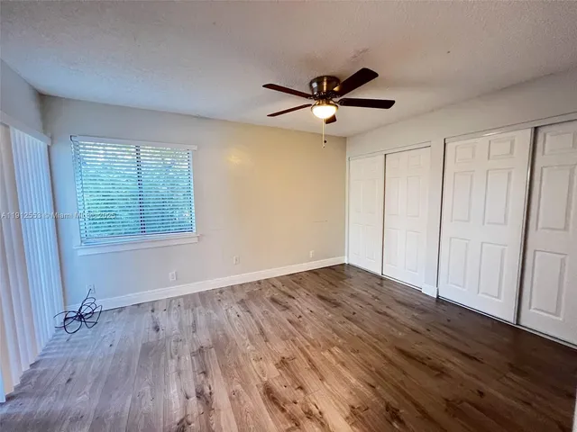 an empty room with wooden floor fan and windows