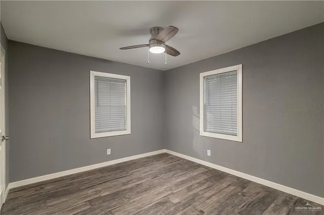 an empty room with wooden floor ceiling fan and windows