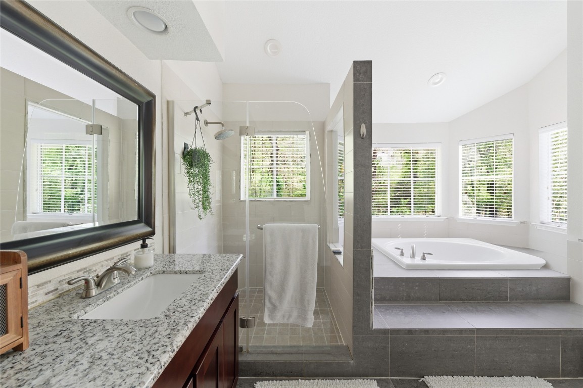 50 East Greywing Circle Spring, TX 77382 - Photo 22 of 37 This spacious bathroom features a glass-enclosed shower, a luxurious corner soaking tub with large windows for natural light, and a sleek granite countertop with a modern sink and vanity.