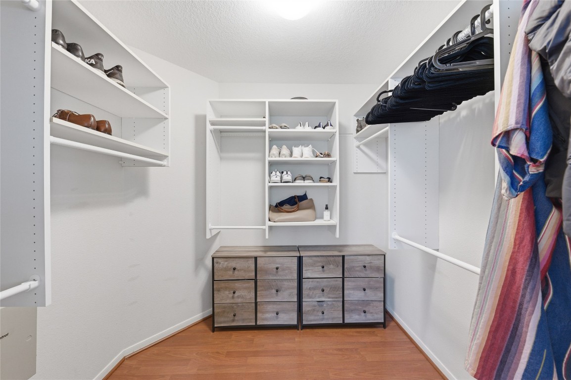 50 East Greywing Circle Spring, TX 77382 - Photo 24 of 37 Spacious walk-in closet with white shelving and rods for ample clothing storage. It features built-in shoe racks, drawers for accessories, and hardwood flooring, making it both functional and stylish.
