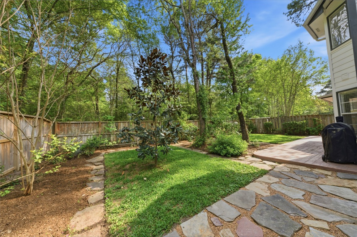 50 East Greywing Circle Spring, TX 77382 - Photo 32 of 37 This backyard features a lush, green lawn with mature trees and shrubs, offering a serene and private setting. A stone path leads to a patio area, perfect for outdoor entertaining, all enclosed by a wooden fence for added privacy.