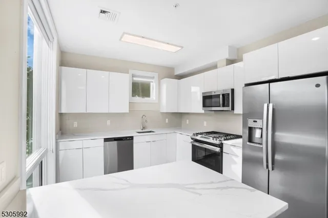 a kitchen with stainless steel appliances kitchen island a refrigerator sink and white cabinets