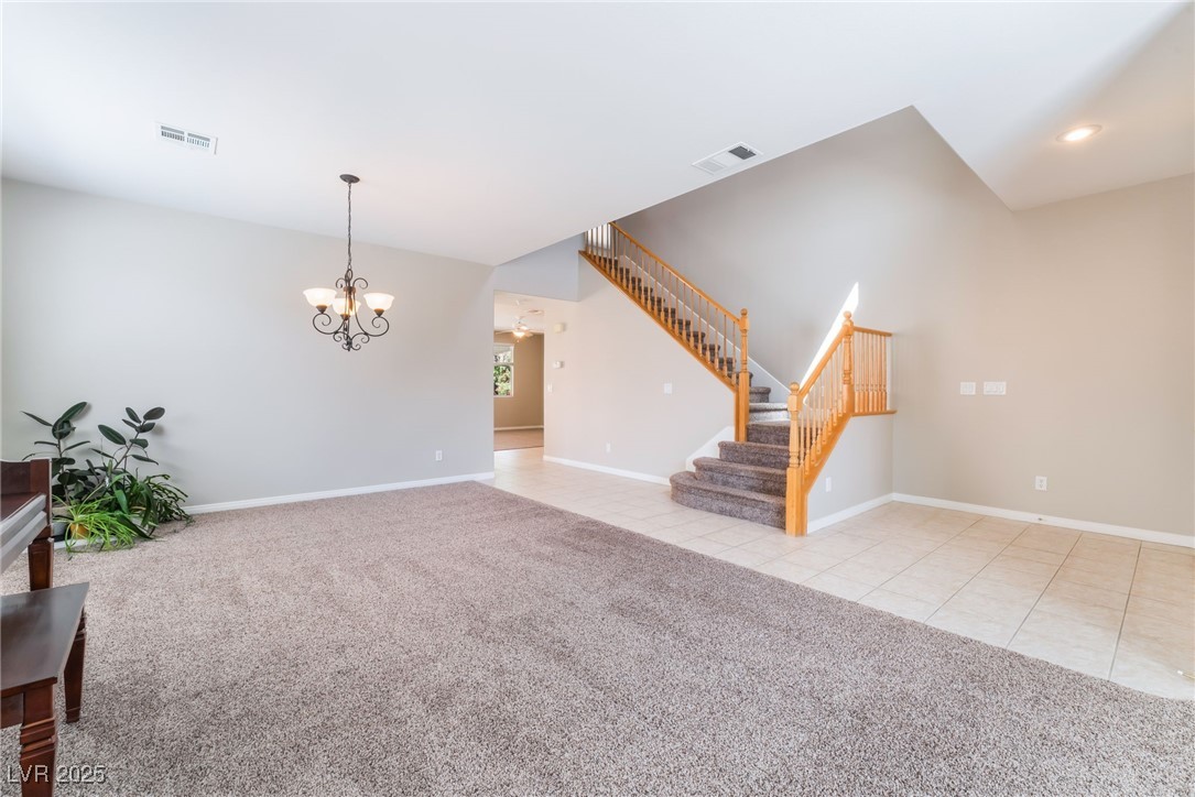 Living room featuring a chandelier, stairway, baseboards, carpet floors, and tile patterned floors