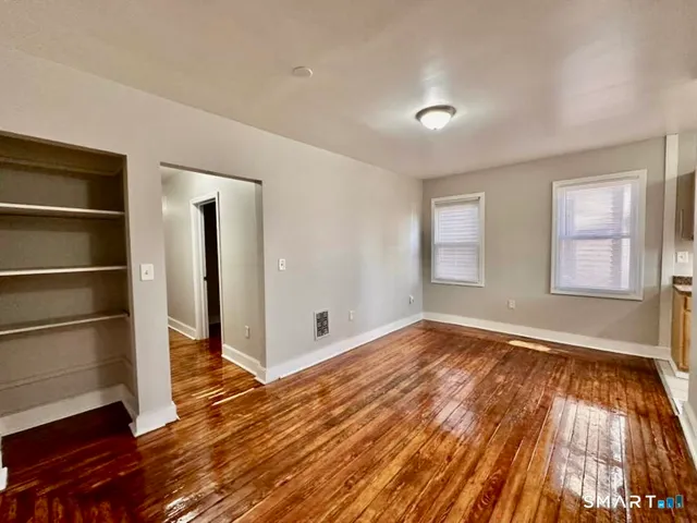 a view of an empty room with wooden floor and window