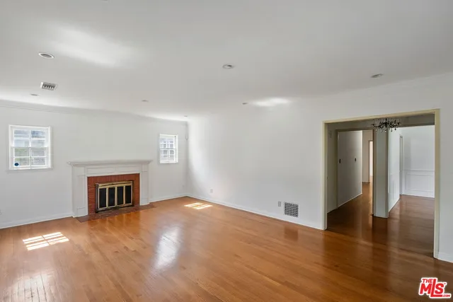 a view of an empty room with wooden floor fireplace and a window