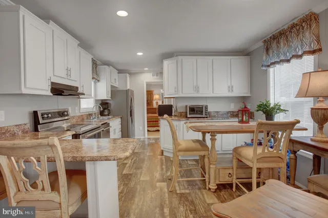 a kitchen with stainless steel appliances granite countertop a stove top oven a sink a refrigerator white cabinets and chairs with wooden floor