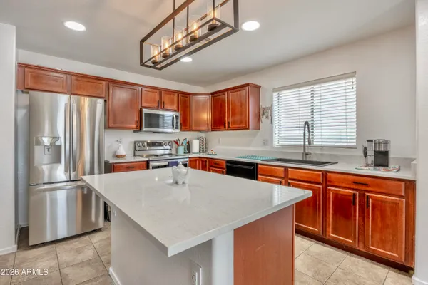 a kitchen with stainless steel appliances granite countertop a refrigerator a sink dishwasher a stove top oven a kitchen island and couches with wooden floor