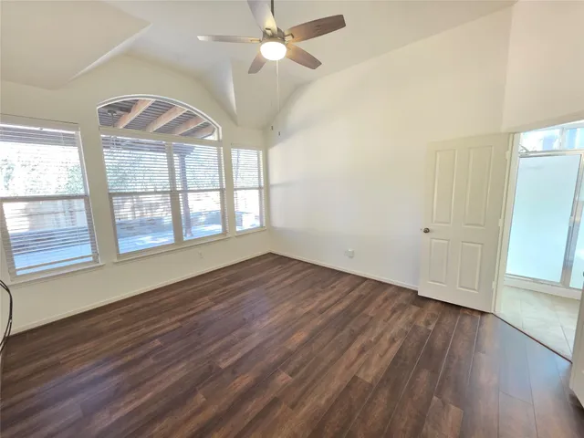 an empty room with wooden floor chandelier fan and windows