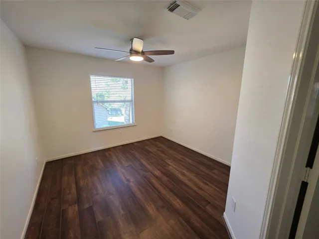 an empty room with wooden floor chandelier fan and windows