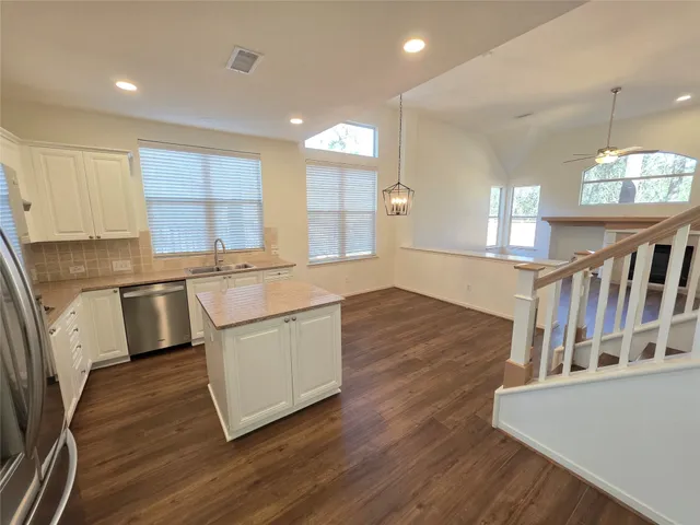 a kitchen with stainless steel appliances granite countertop a sink a stove a refrigerator cabinets and a wooden floor