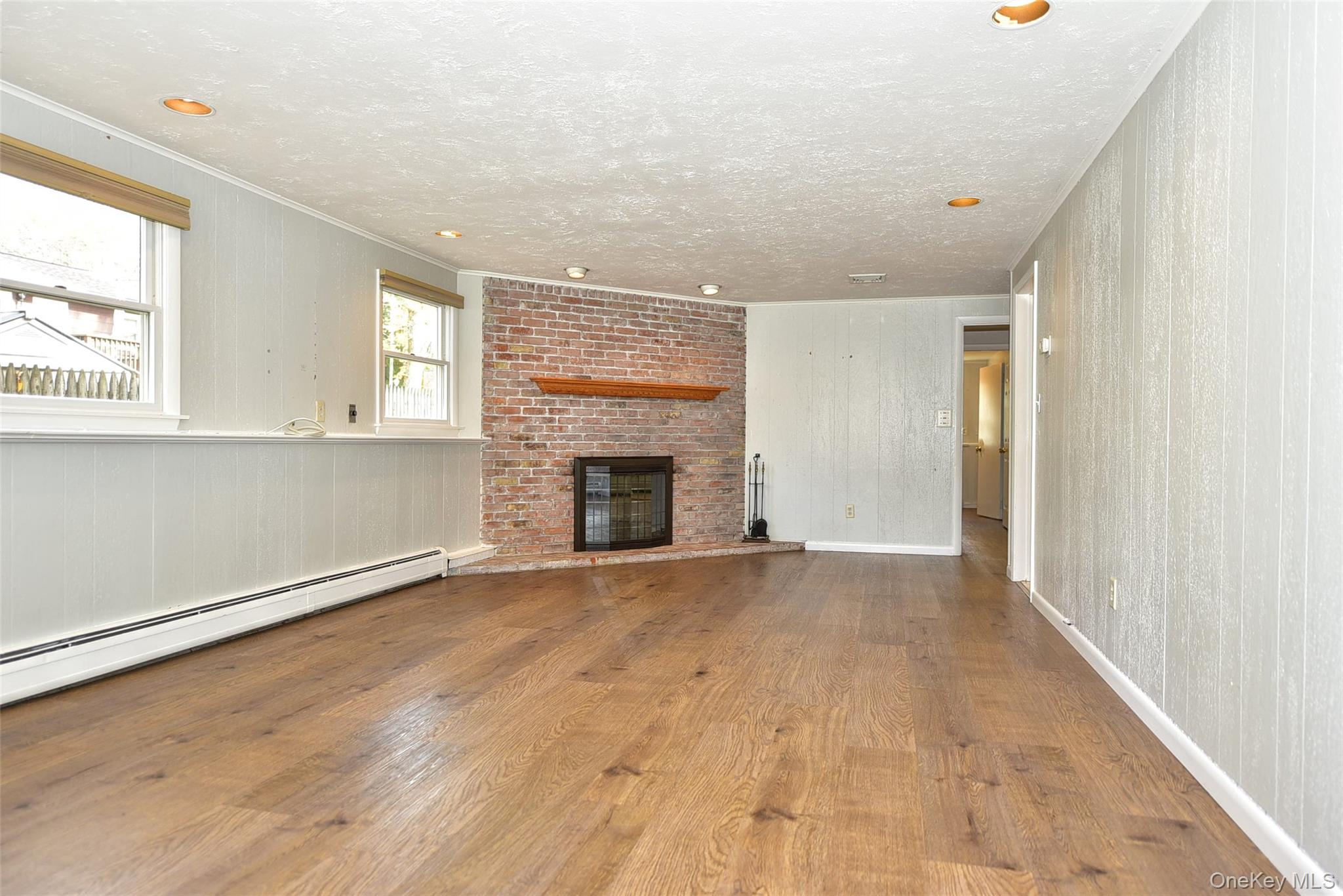 33 Hillcrest Road Suffern, NY 10901 - Photo 24 of 39 Unfurnished living room featuring wood finished floors, a fireplace, baseboard heating, crown molding, and a textured ceiling