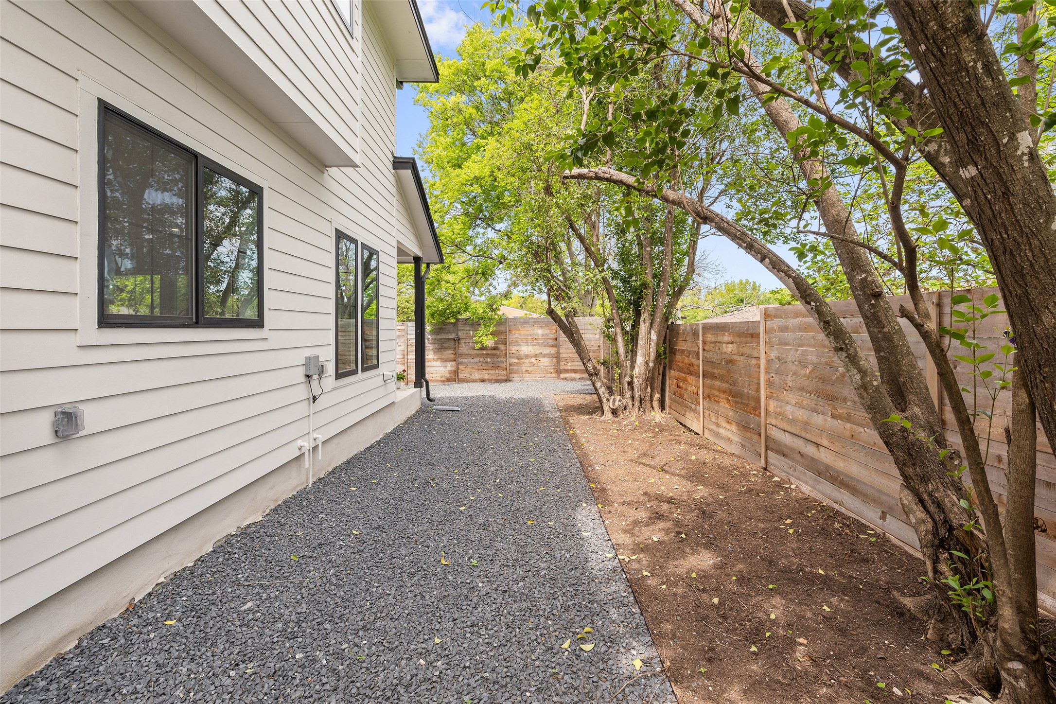 1504 Ruth Avenue, Unit 3 Austin, TX 78757 - Photo 34 of 39 A private outdoor space with a wooden privacy fence, trees, and a gravel walkway.