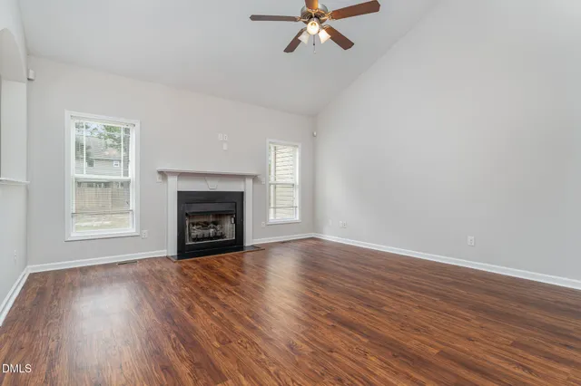 a view of an empty room with wooden floor fireplace and a window