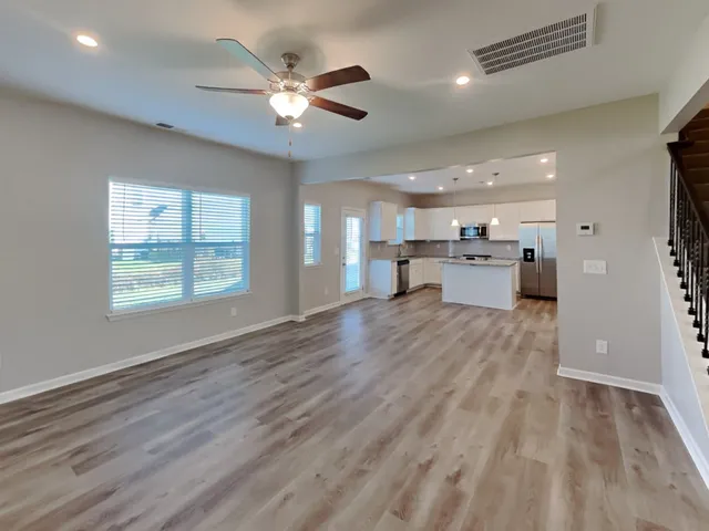 an empty room with wooden floor a ceiling fan and windows