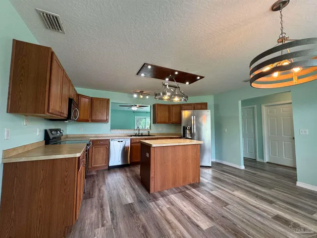 a kitchen with stainless steel appliances granite countertop a sink dishwasher a stove and a refrigerator with wooden floor