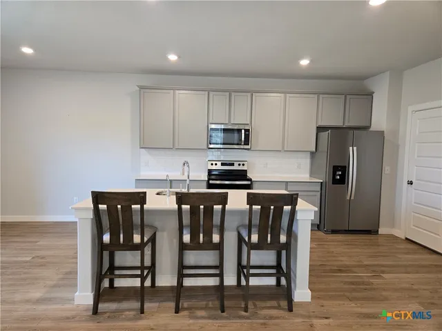 a kitchen with stainless steel appliances granite countertop a dining table chairs refrigerator and microwave