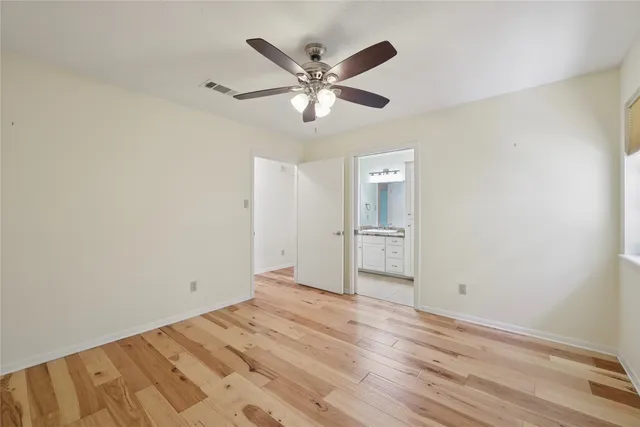 a view of an empty room with wooden floor and a ceiling fan