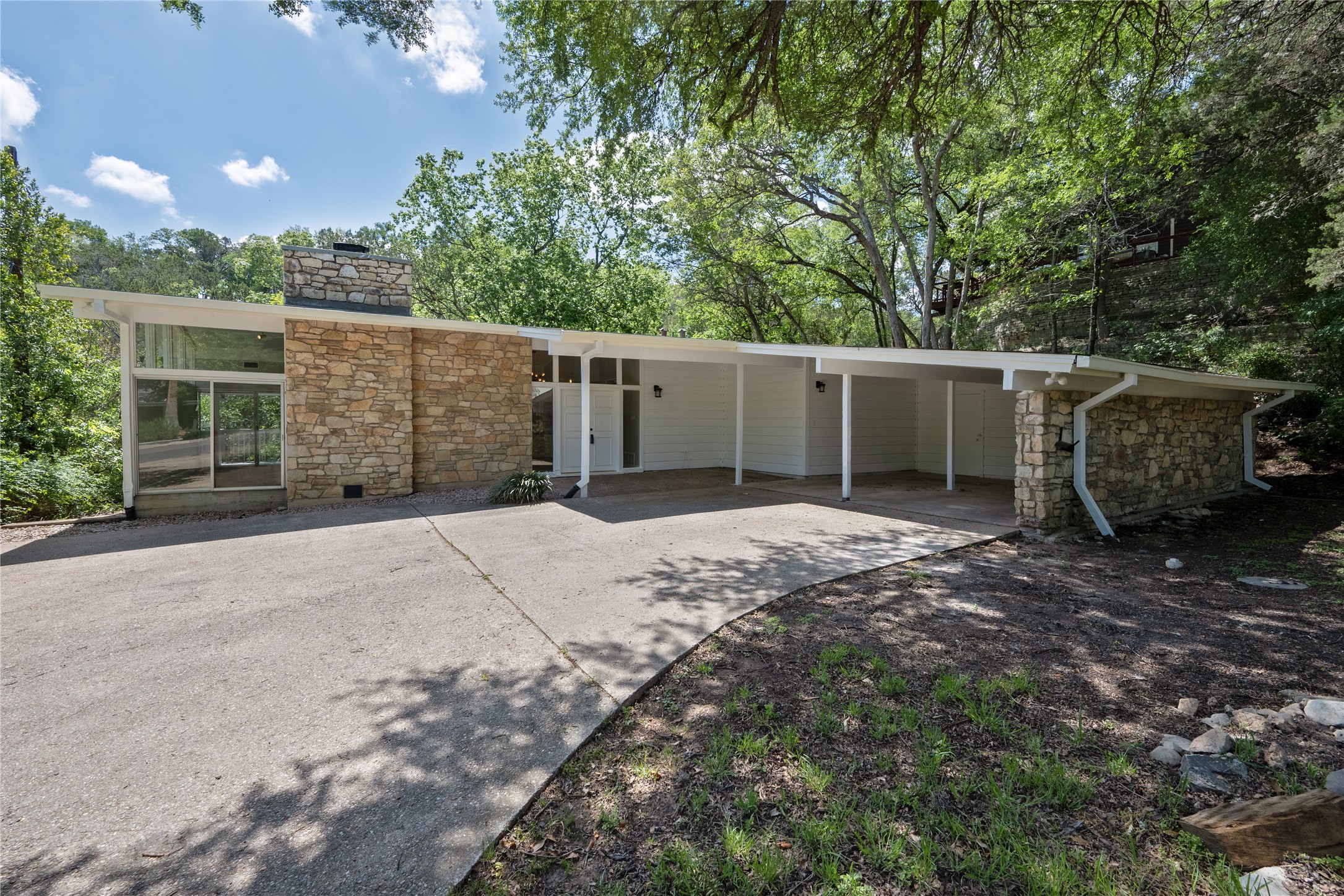 7 Hull Circle Austin, TX 78746 - Photo 1 of 17 A striking mid-century modern home nestled in a lush, tree-filled landscape, featuring a carport and stone accents.