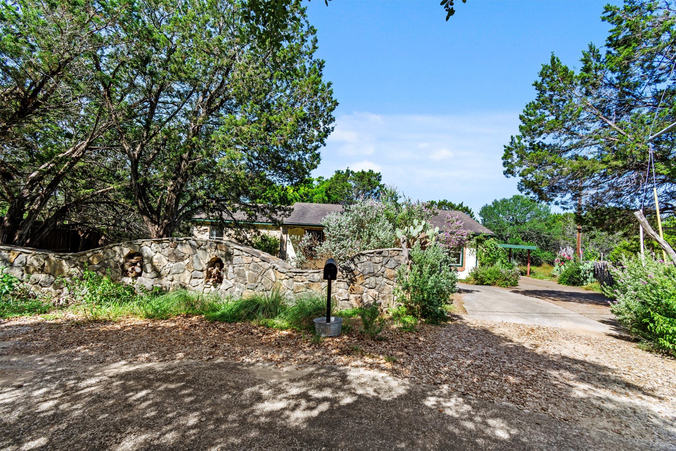 6 El Sol Road Wimberley, TX 78676 - Photo 2 of 20 A stone wall entrance leads to a charming residence nestled amidst mature trees.