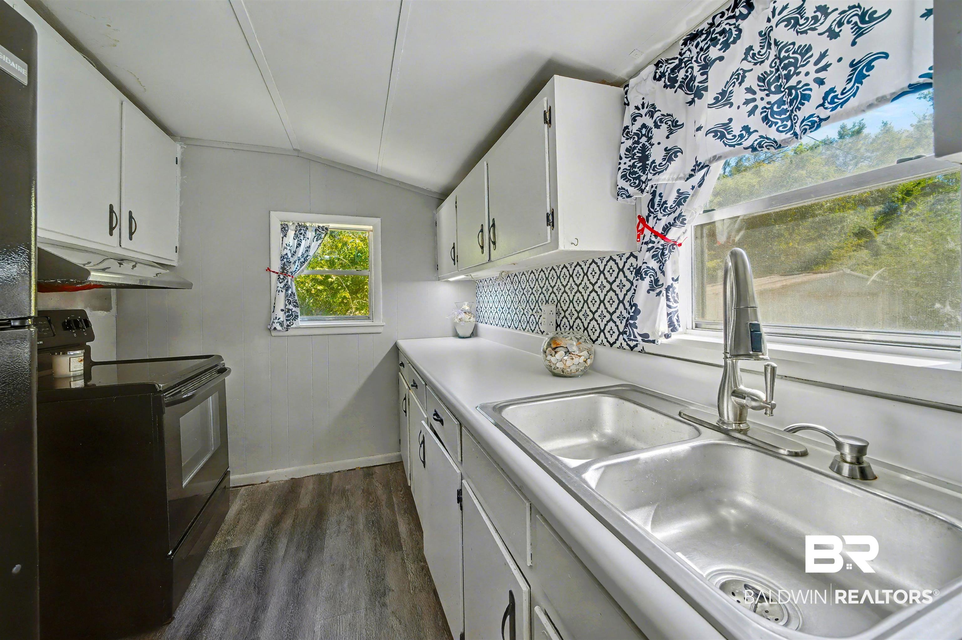 209 West Magnolia Avenue Foley, AL 36535 - Photo 20 of 23 Kitchen with dark wood-type flooring, black appliances, white cabinetry, lofted ceiling, and light countertops