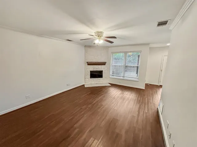 an empty room with wooden floor ceiling fan and windows