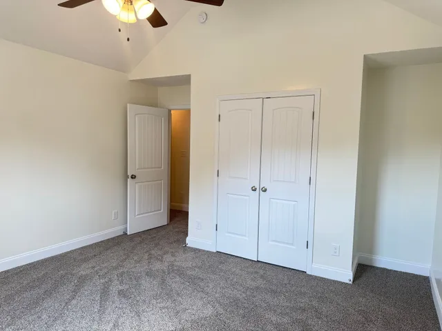 an empty room with a chandelier fan and closet area