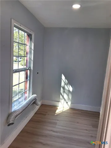 a view of an empty room with wooden floor and a window