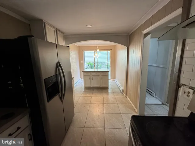 a view of a refrigerator in kitchen and an empty room in wooden floor