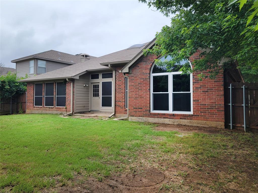 1604 Knoll Ridge Circle Corinth, TX 76210 - Photo 37 of 37 Rear exterior featuring brick and horizontal siding, an arched window, multiple window screens, a back door with surrounding transom and sidelight windows, and a wood privacy fence