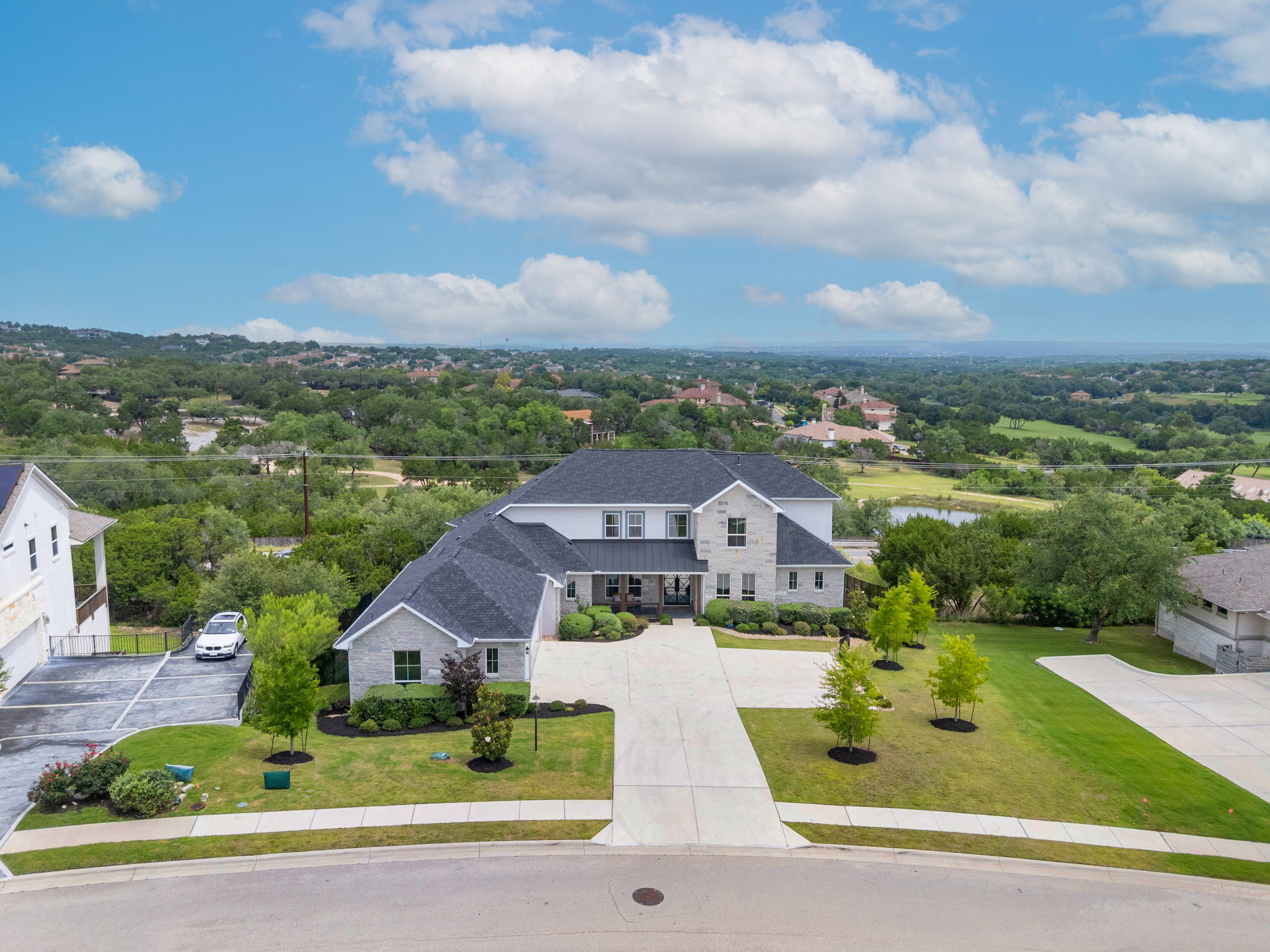 104 Lodestone Cove Austin, TX 78738 - Photo 37 of 40 An impressive two-story residence with a stone facade and a wide driveway, nestled on a landscaped lot with distant views.