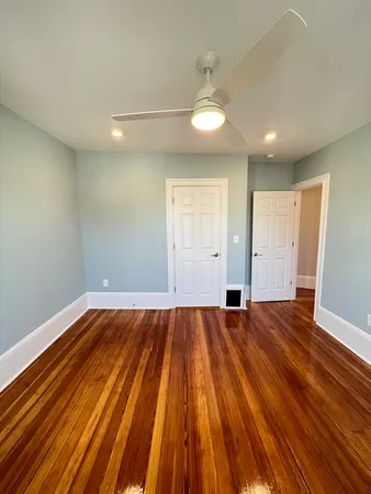 a view of an empty room with wooden floor and a ceiling fan