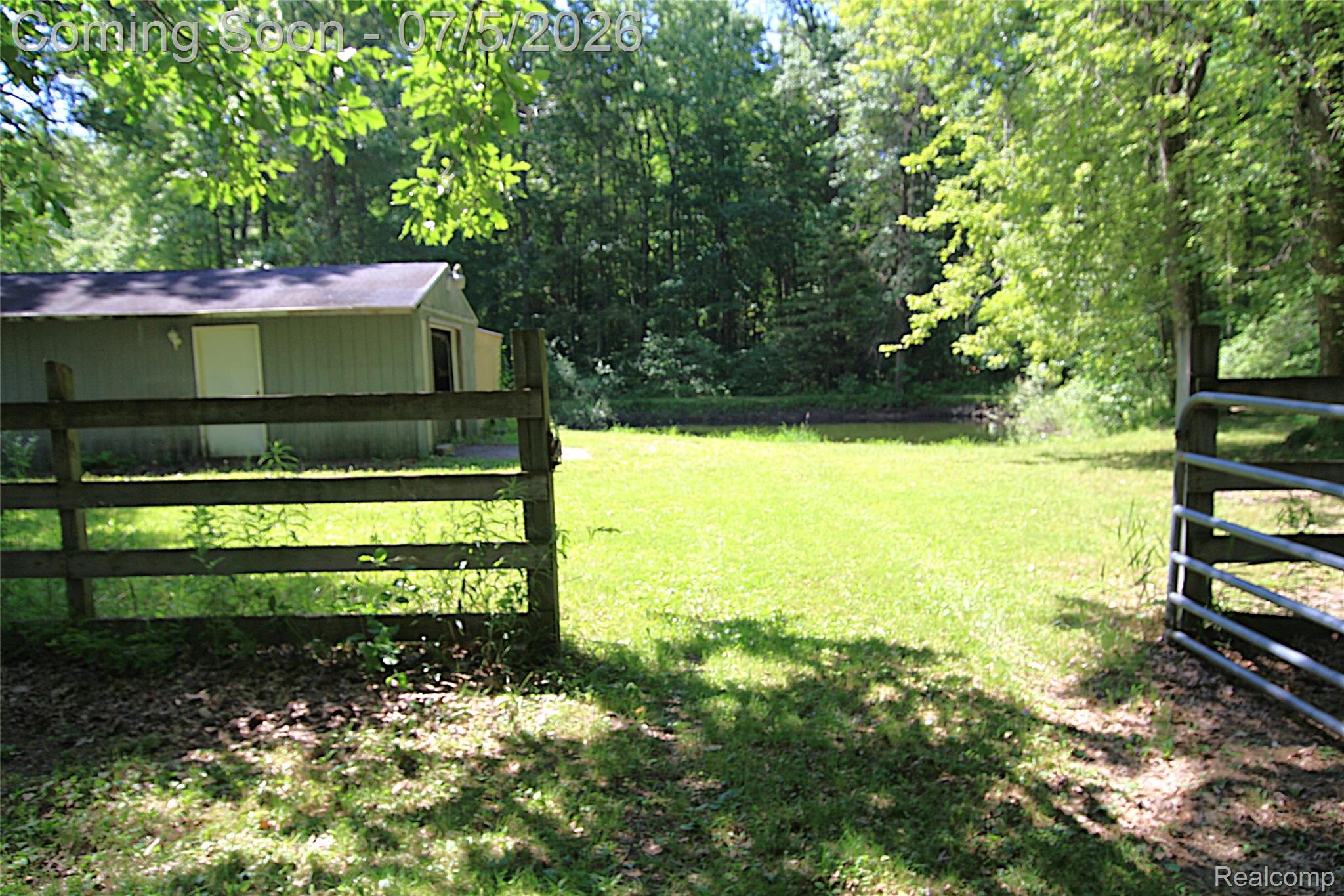 12403 Willard Road Montrose, MI 48457 - Photo 7 of 30 Expansive green space featuring a wood fence, a metal gate, and a storage shed with a shingled roof