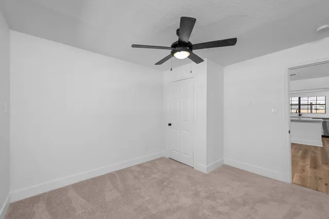 an empty room with wooden floor chandelier fan and windows