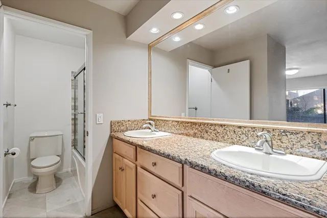 a bathroom with a granite countertop double vanity sink a mirror and a toilet