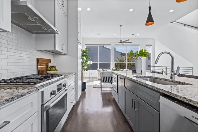a kitchen with kitchen island granite countertop a stove a sink dishwasher and white cabinets with wooden floor
