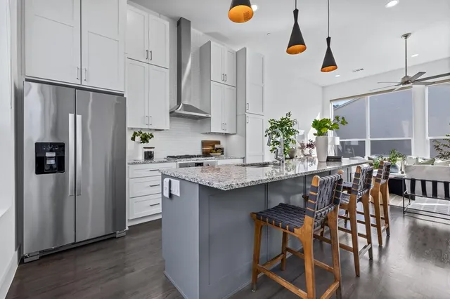 a kitchen with stainless steel appliances granite countertop a refrigerator a sink dishwasher a stove a dining table and chairs with wooden floor