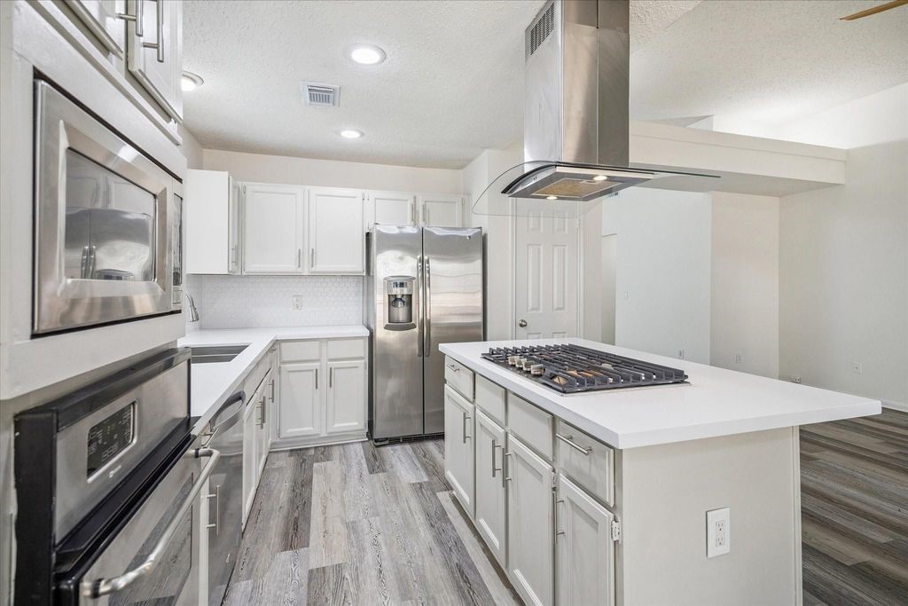143 West Village Knoll Circle Spring, TX 77381 - Photo 10 of 27 This beautifully updated kitchen boasts stainless steel appliances, a gas cooktop with sleek vent hood, ovens, and an island for cooking and entertaining. Crisp white cabinetry, modern backsplash, and durable wood-look flooring complete the fresh, contemporary design.