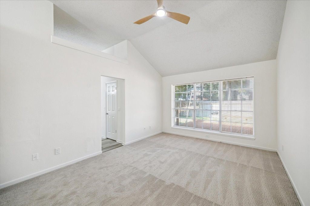 143 West Village Knoll Circle Spring, TX 77381 - Photo 21 of 27 Spacious primary suite with vaulted ceilings, plush carpet, and a wall of windows overlooking the backyard—creating a bright and relaxing retreat.