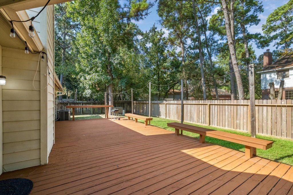 143 West Village Knoll Circle Spring, TX 77381 - Photo 26 of 27 This angle showcases the expansive wooden deck with built-in seating, perfect for entertaining or relaxing outdoors. The fully fenced yard offers privacy, while mature trees provide shade and a welcoming backdrop.