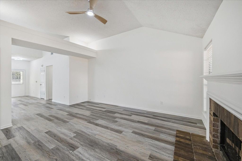 143 West Village Knoll Circle Spring, TX 77381 - Photo 7 of 27 This open-concept living area seamlessly blends comfort and functionality with a cozy brick fireplace, high ceilings, and wood-look flooring. The adjacent modern kitchen features a large island, sleek vent hood, and ample natural light—perfect for entertaining or everyday living.