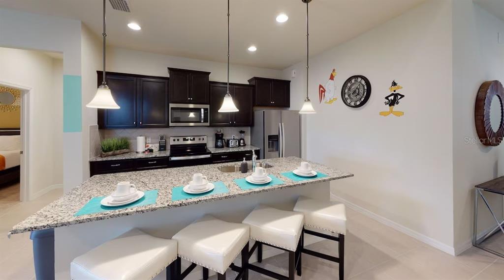 2479 Dubai Street Kissimmee, FL 34747 - Photo 14 of 70 a kitchen with stainless steel appliances granite countertop a sink a stove a refrigerator a dining table and chairs with wooden floor