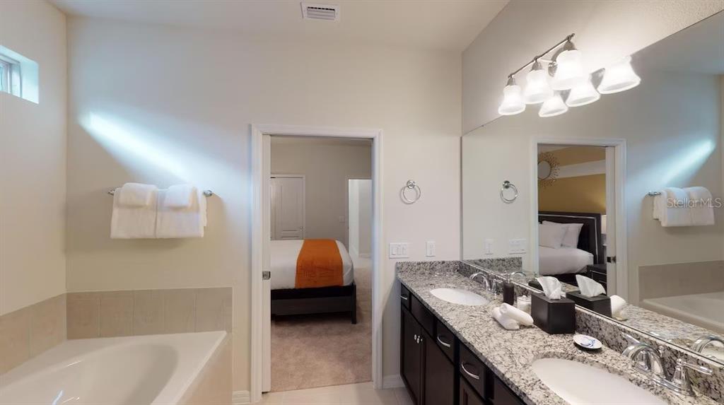 2479 Dubai Street Kissimmee, FL 34747 - Photo 32 of 70 a en suite bathroom with a granite countertop sink a large mirror and a bathtub