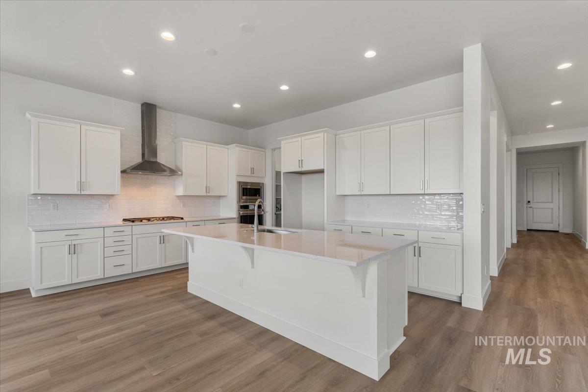 929 North Falling Water Way Eagle, ID 83616 - Photo 17 of 43 Kitchen with white cabinetry, a kitchen breakfast bar, tasteful backsplash, wall chimney range hood, and an island with sink