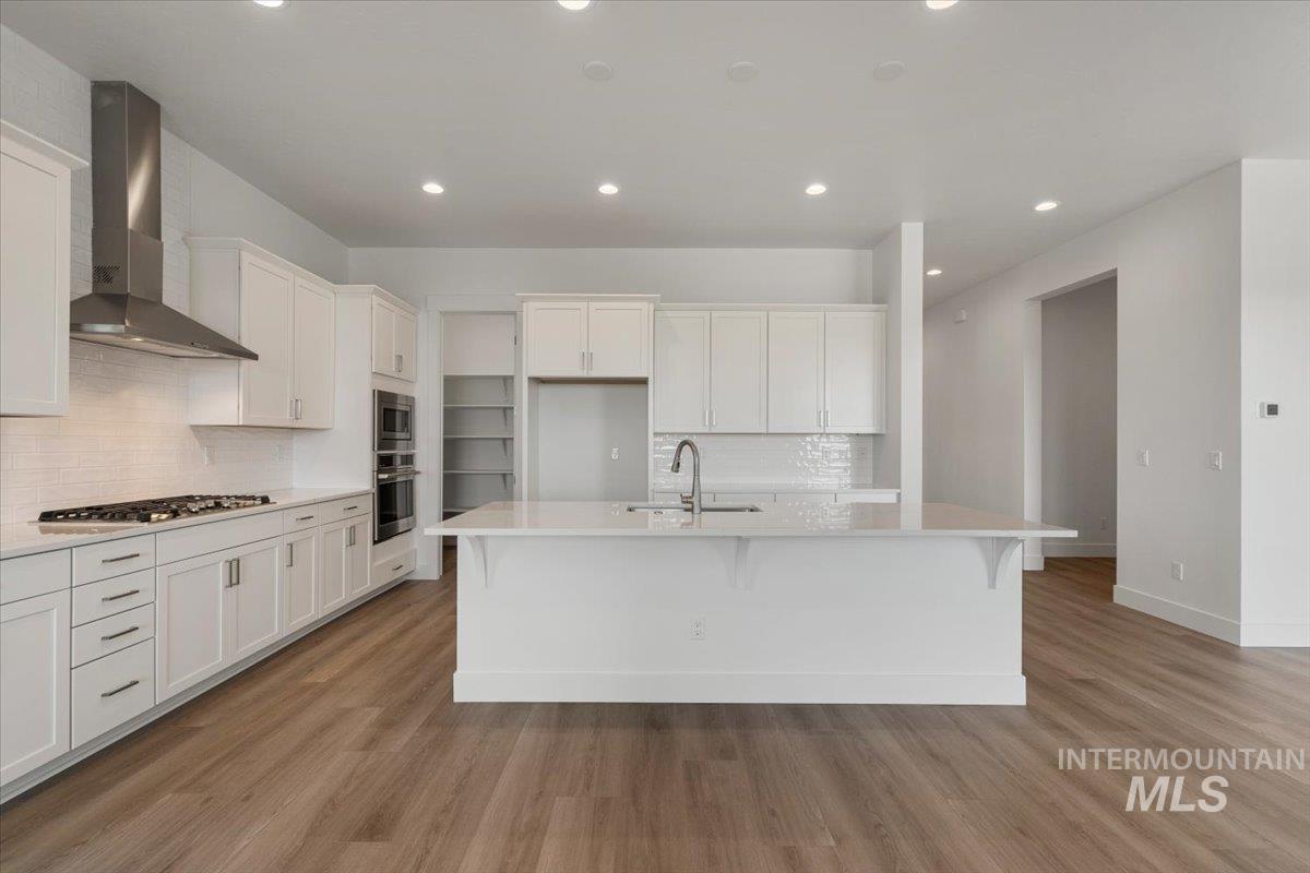 929 North Falling Water Way Eagle, ID 83616 - Photo 18 of 43 Kitchen featuring backsplash, wall chimney range hood, white cabinetry, recessed lighting, and light wood-type flooring
