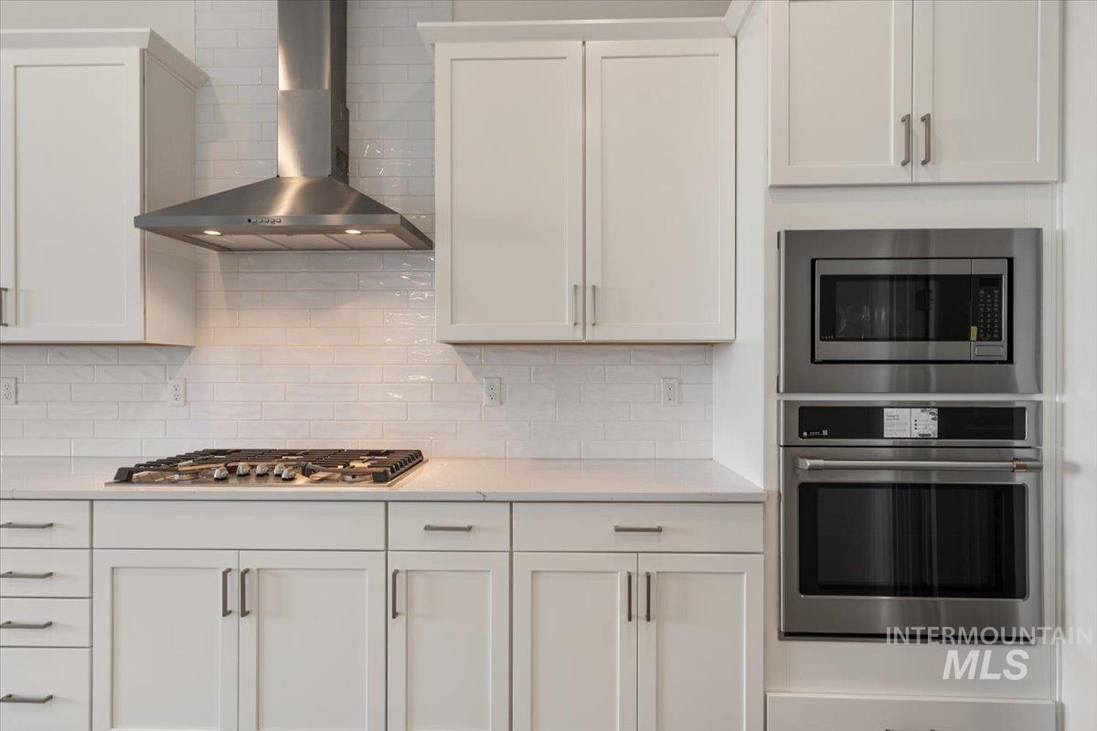 929 North Falling Water Way Eagle, ID 83616 - Photo 20 of 43 Kitchen with wall chimney range hood, stainless steel appliances, white cabinets, and decorative backsplash