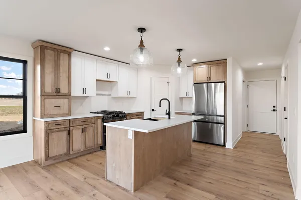 a kitchen with stainless steel appliances granite countertop a refrigerator a stove a sink and white cabinets with wooden floor