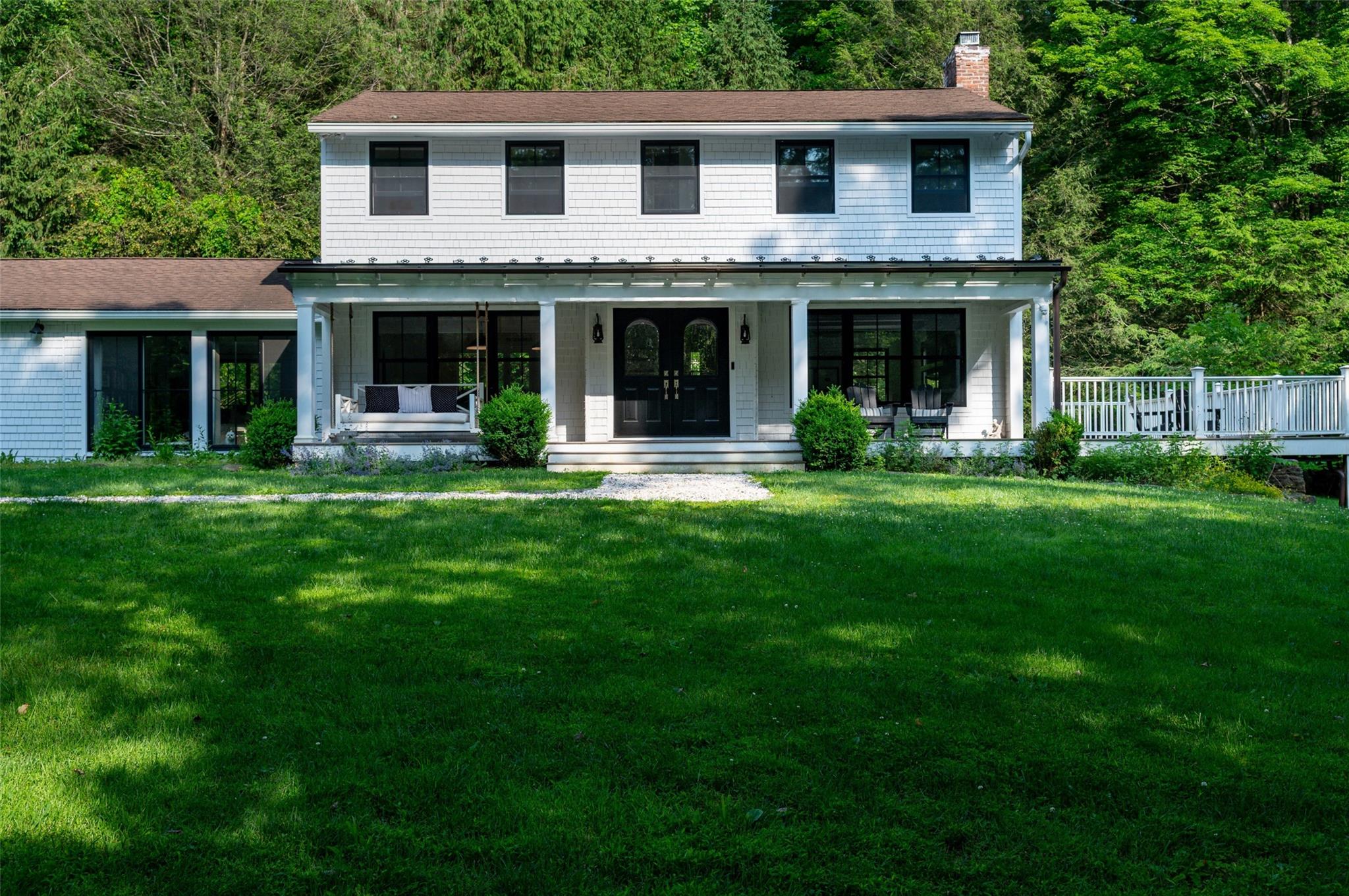 View of front of property with a chimney, a porch, a front yard, and a view of trees