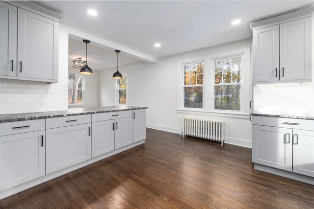 a kitchen with granite countertop a stove a sink and white cabinets with wooden floor