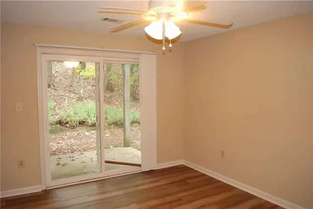 a view of an empty room with wooden floor and fan