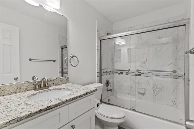 a bathroom with a granite countertop sink a mirror a shower and a toilet